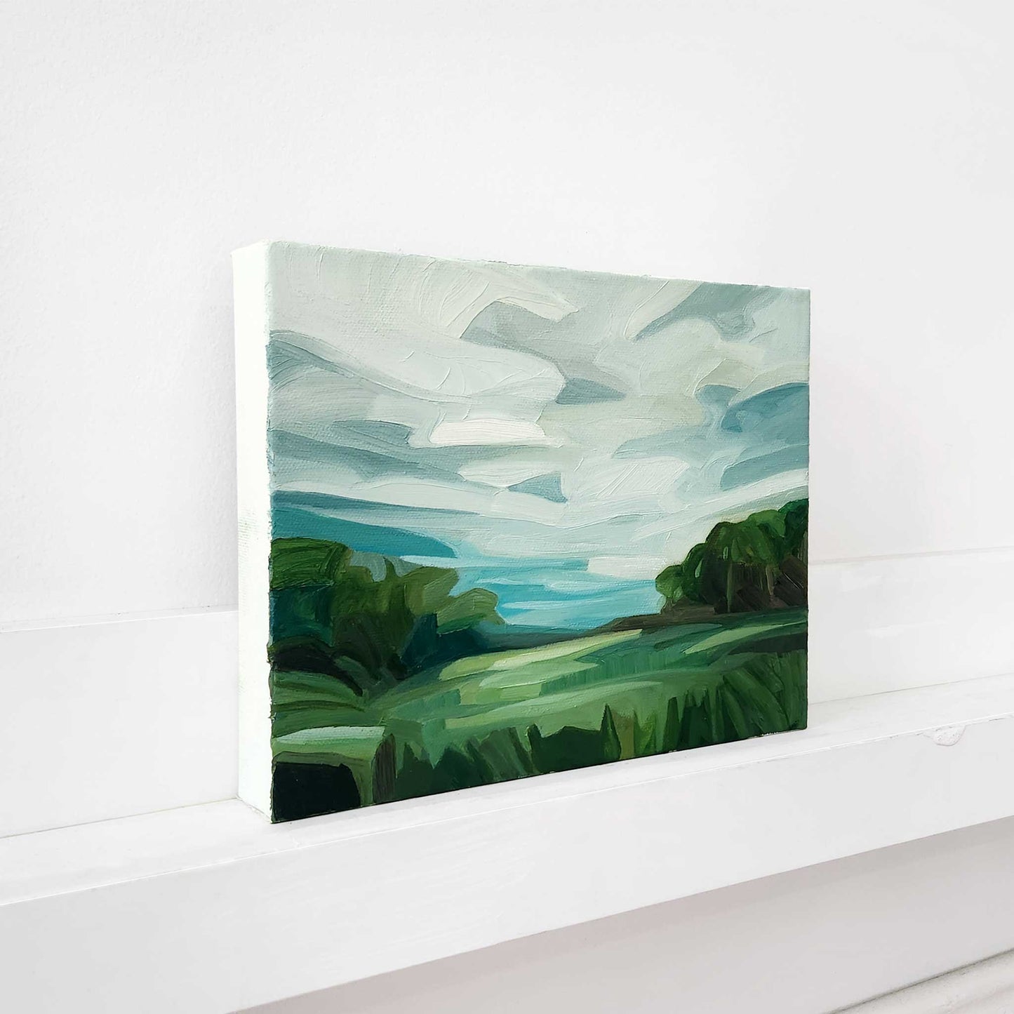 Original countryside painting with forest views and vibrant green fields.
