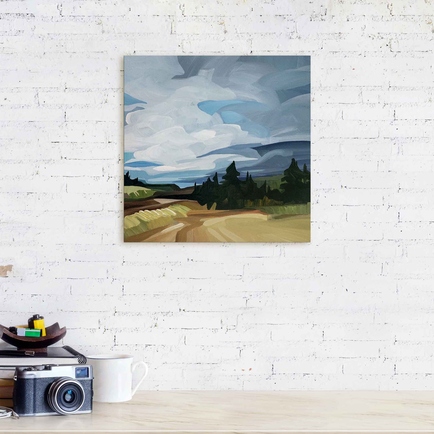 abstract landscape painting on canvas with big blue sky hanging over counter against white brick wall