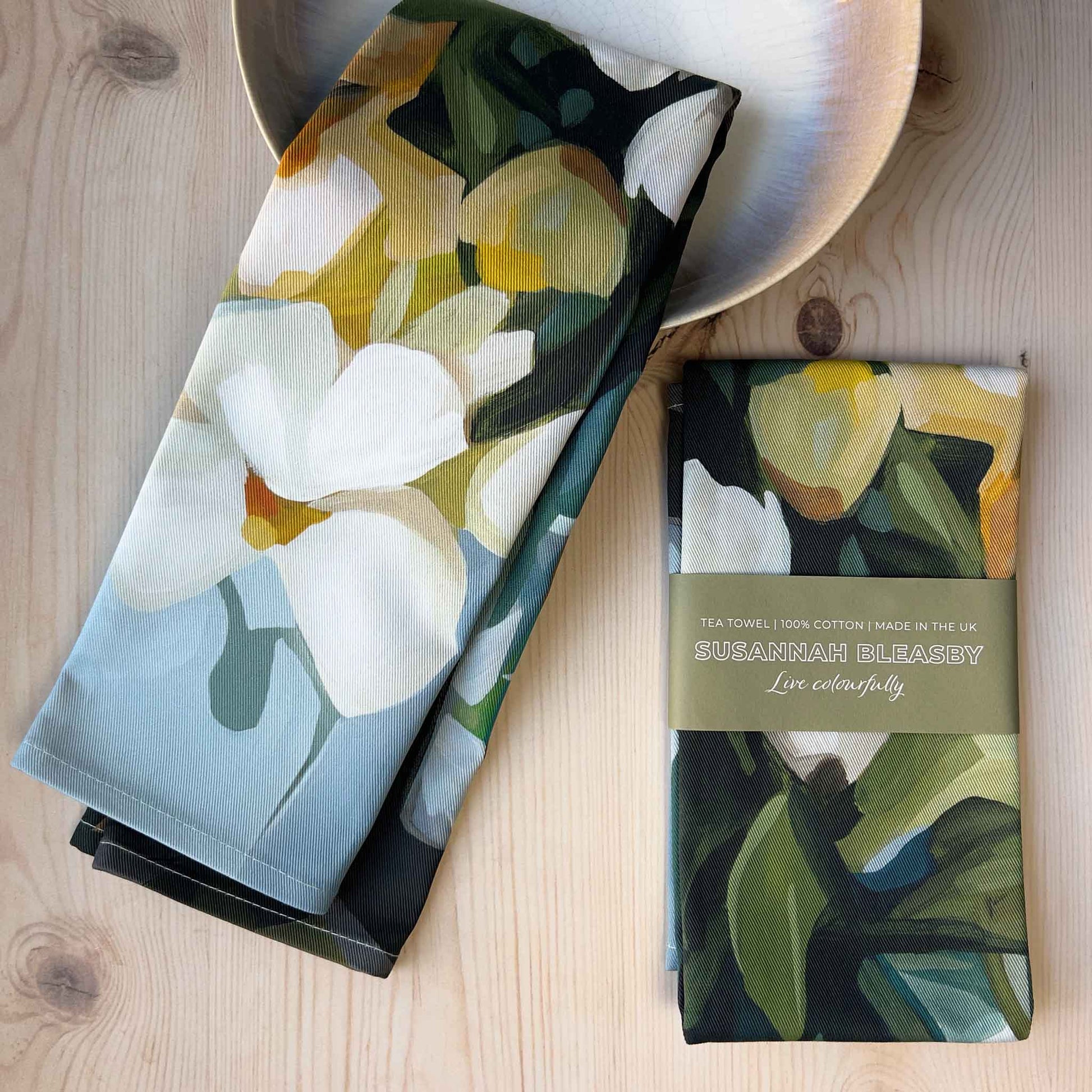 british made cotton tea towel with cream and yellow flowers folded on a wooden table