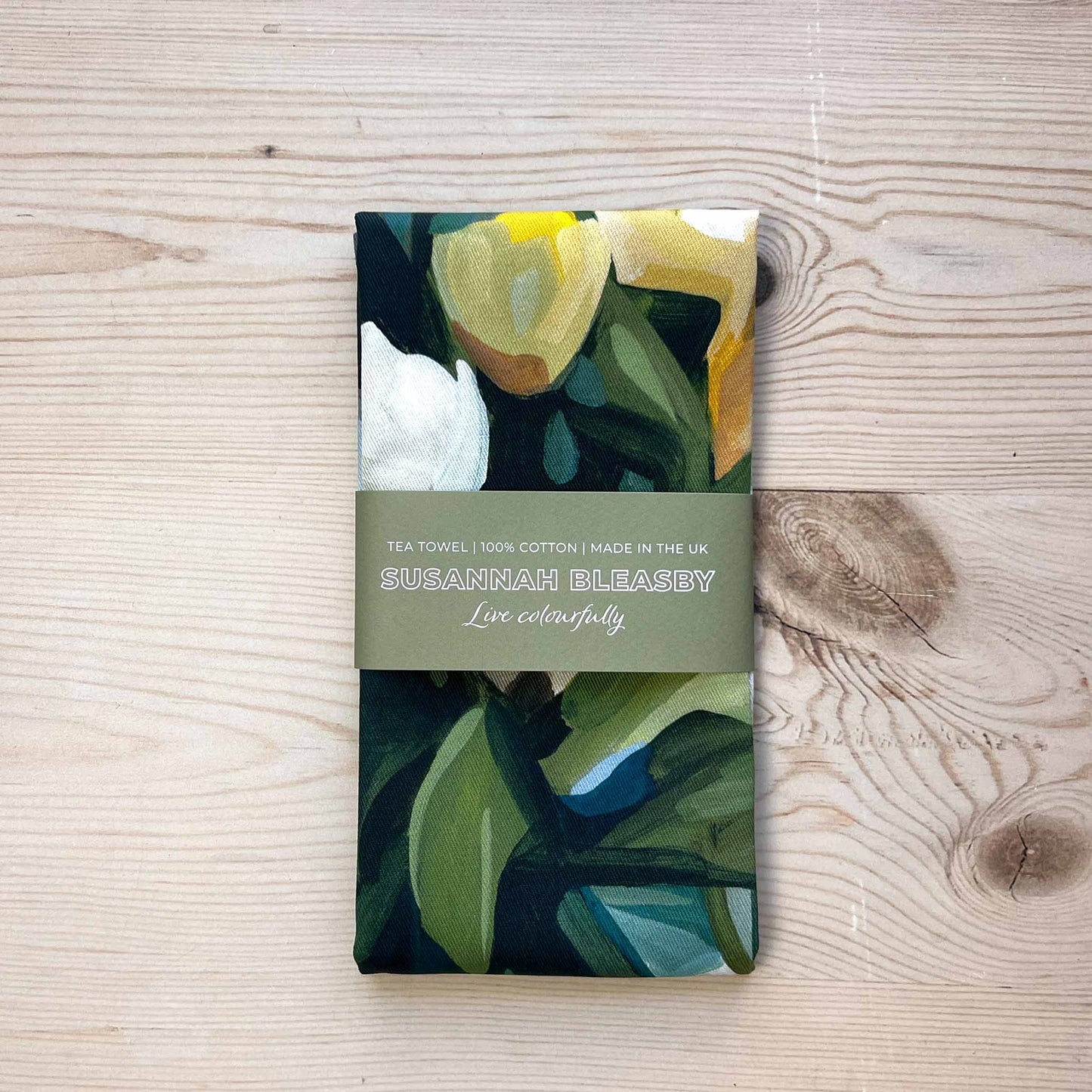 british made floral tea towel with yellow and cream flowers folded on a wooden table