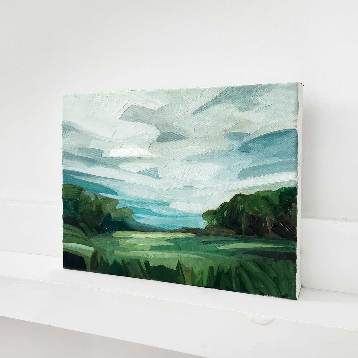 Landscape oil painting of green fields leading towards a peaceful woodland.