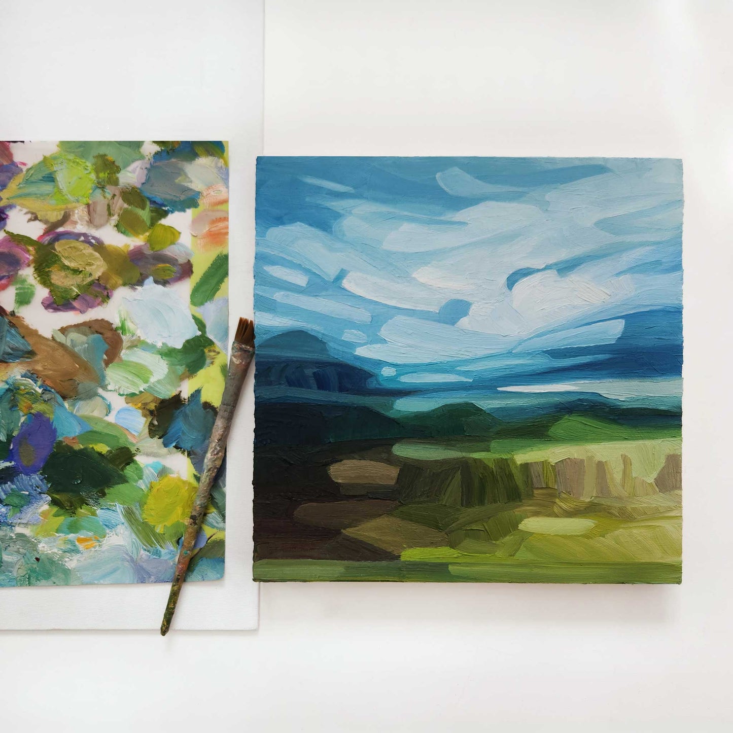 overhead view of an original oil painting of an abstract spring landscape with a bright blue sky and sweeping clouds over green hills in the countryside
