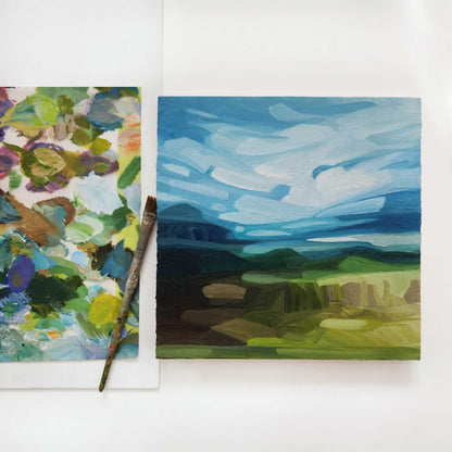 overhead view of an original oil painting of an abstract spring landscape with a bright blue sky and sweeping clouds over green hills in the countryside