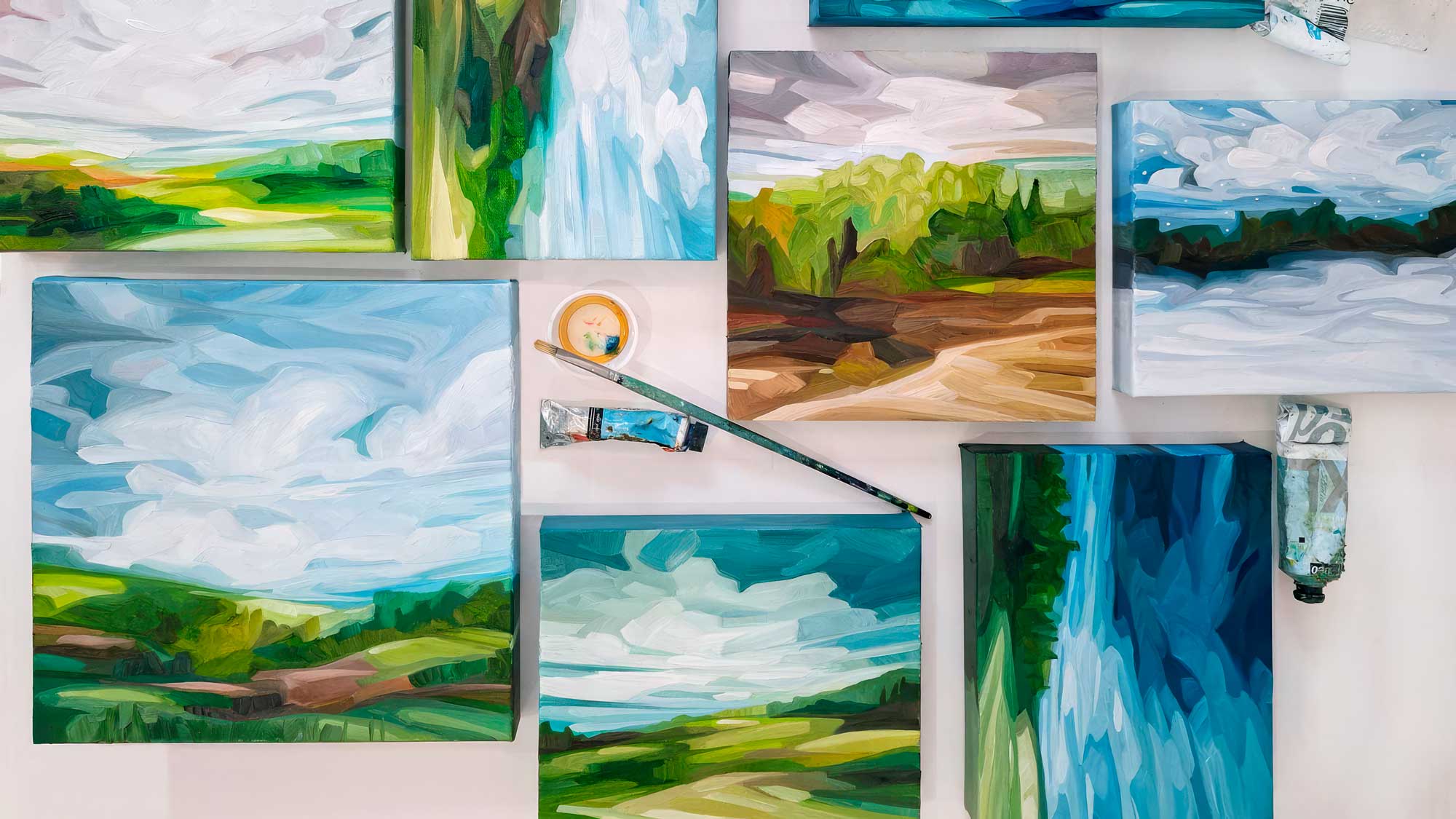 collection of landscape oil paintings with paintbrush on artist bench