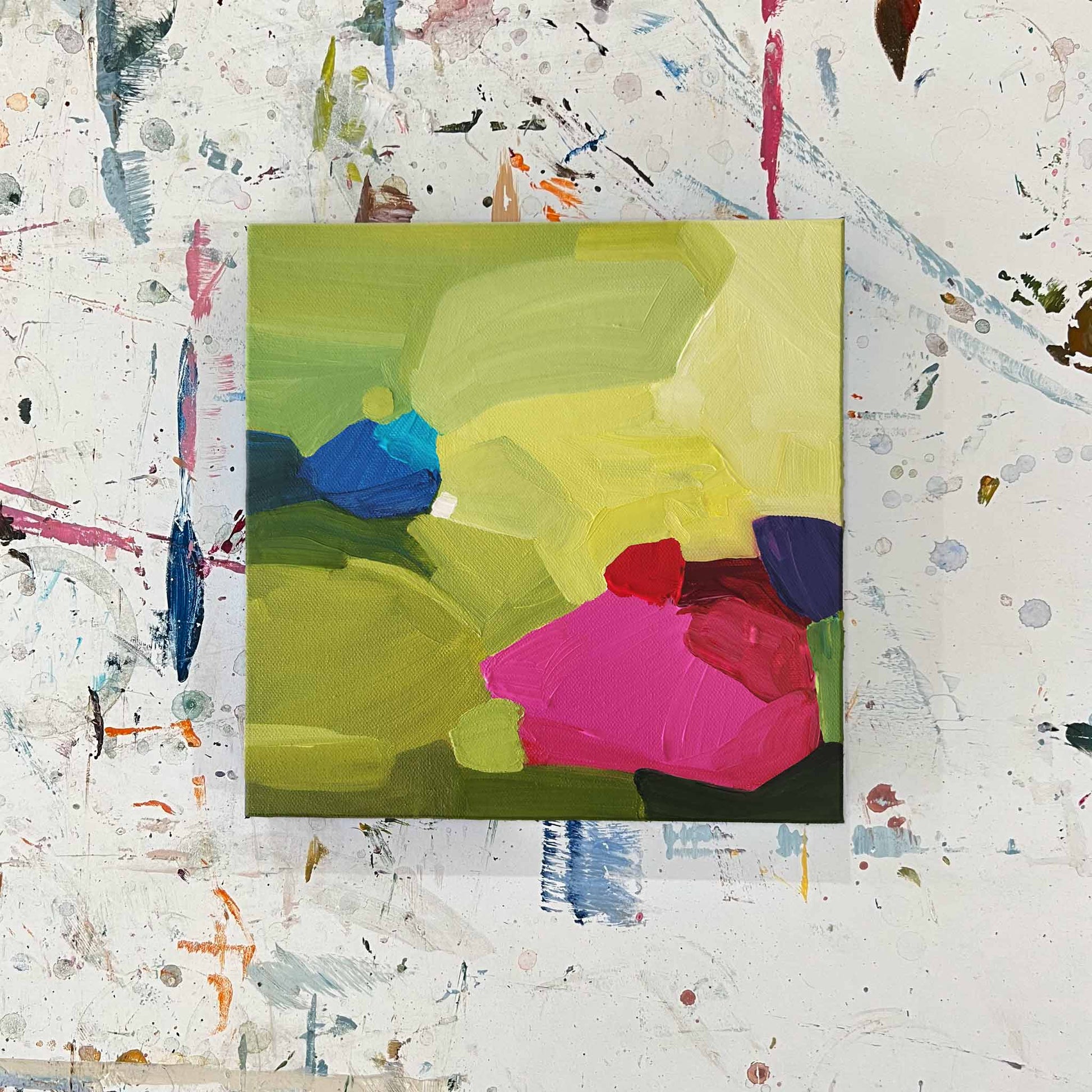 Top view of a small abstract painting with bright pink and blue shapes on a lime green background by Canadian abstract artist Susannah Bleasby
