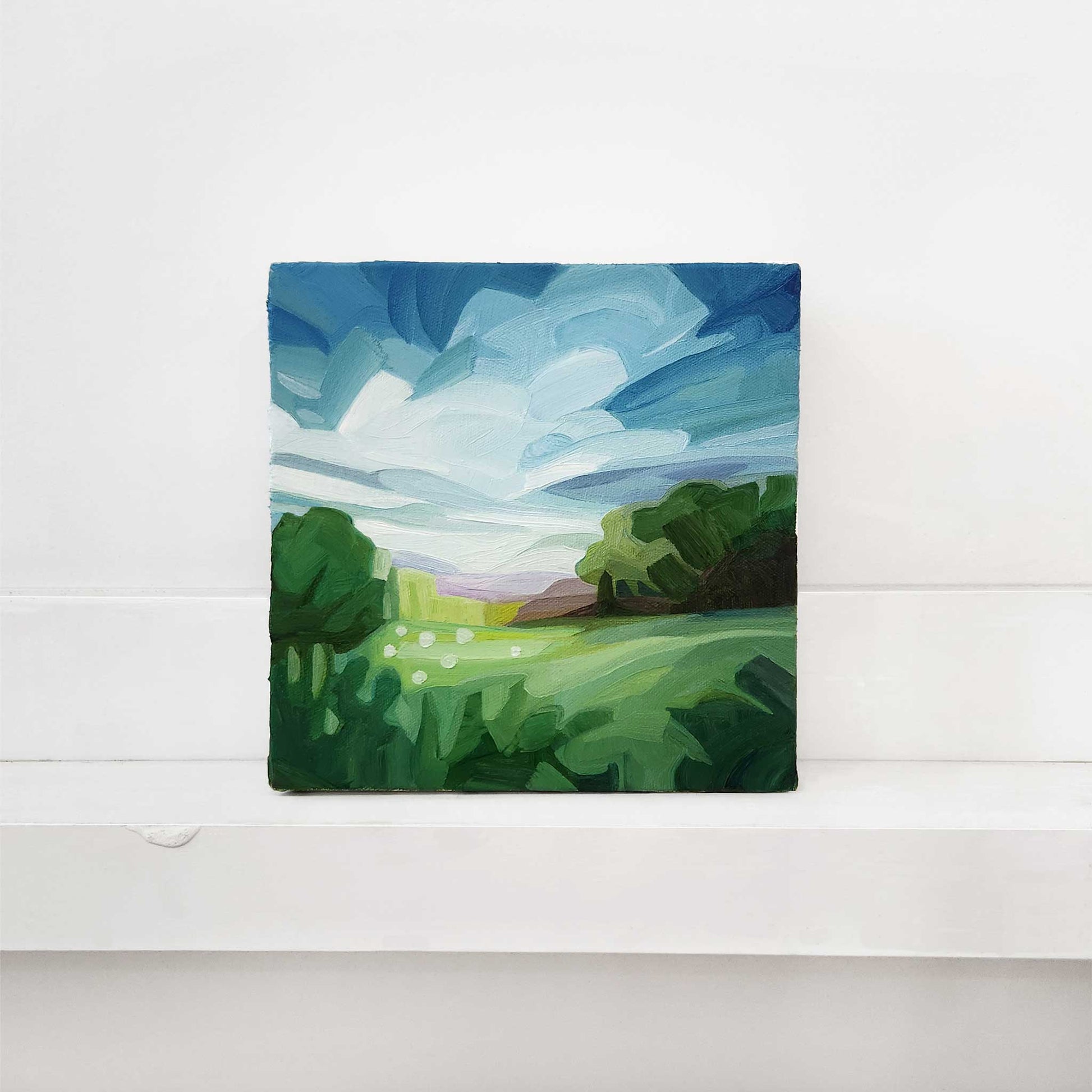 Original oil painting of a peaceful green meadow landscape beneath a bright blue sky.