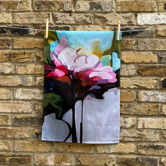 pink floral cotton tea towel hanging against a brick wall