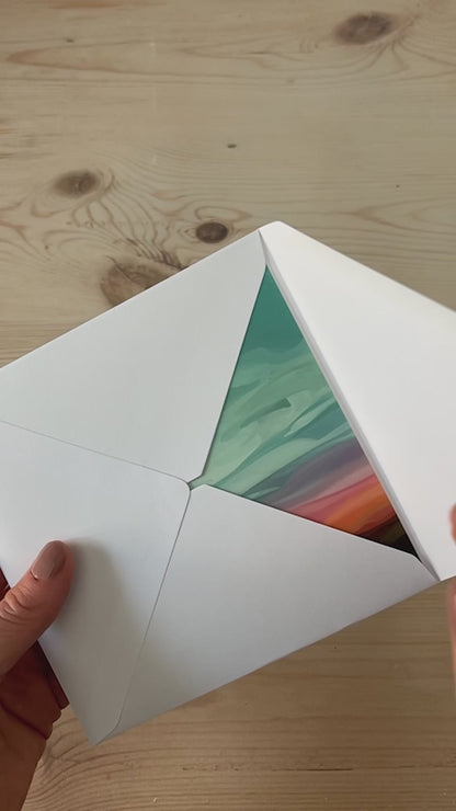Abstract sky greeting card being opened from a white envelope with glowing sunset cloudscape artwork
