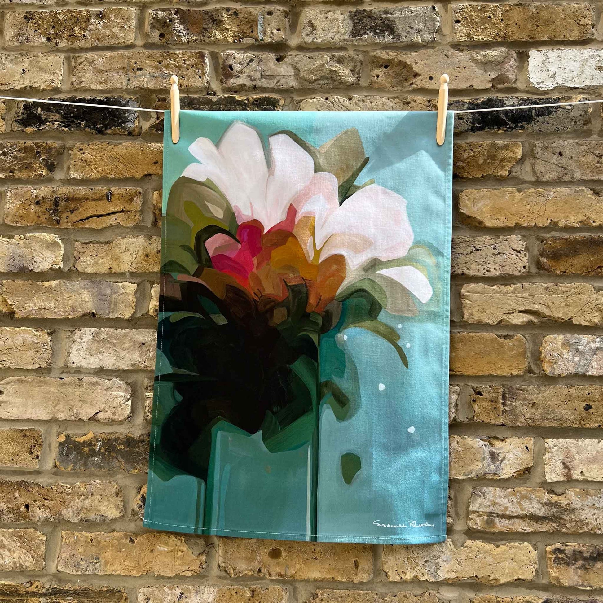 teal cotton tea towel hanging against a brick wall