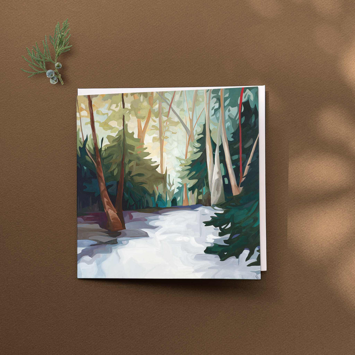 Winter landscape greeting card featuring a snowy forest, glowing sunlight and a winding woodland path