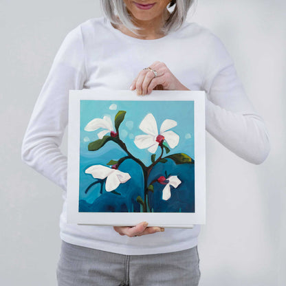 Canadian artist Susannah Bleasby holding one of her floral art prints featuring small white flowers on a white background