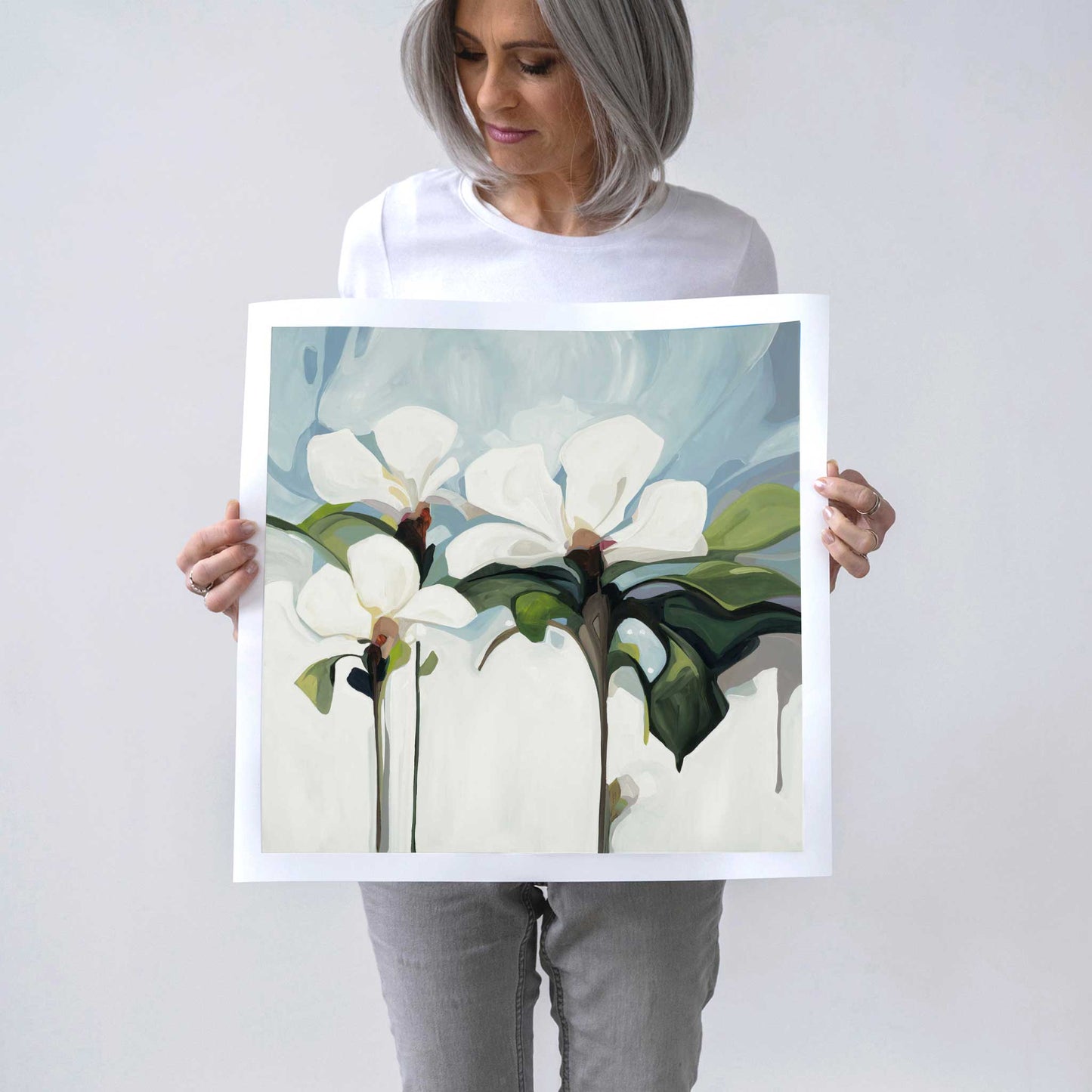 Canadian artist Susannah Bleasby holding 20x20 art print of an acrylic flower painting with white flowers on a light blue background