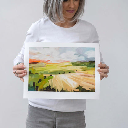 canadian abstract artist Susannah Bleasby holding a horizontal abstract landscape art print of a countryside view